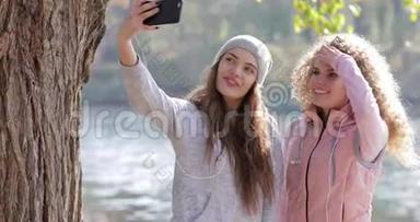 两个漂亮的小女孩在手机上拍照，靠近树户外日出，早秋公园