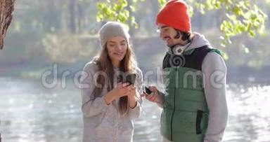 年轻夫妇男人和漂亮女人使用手机户外日出，早秋公园