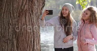 两个漂亮的小女孩在手机上拍照，靠近树户外日出，<strong>早秋</strong>公园