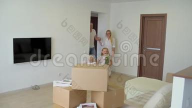 年轻幸福的家庭搬到新公寓。 两个小女孩和父母一起跑进新家的背景纸板
