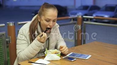 一位中年白人妇女在一个寒冷的夜晚坐在一家夏季咖啡馆的桌子旁，吃蔬菜沙拉和油炸食品