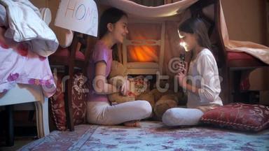 两个姐妹坐在卧室的毯子下面，用手电筒<strong>讲故事</strong>