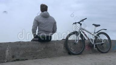 一个骑自行车的人在大风暴中坐在旧的高混凝土码头上。