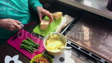 女人在切割板上切奶酪。 <strong>接下来</strong>的盘子是葱，土豆泥和炸蘑菇。