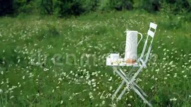 在洋甘菊的草坪中矗立着<strong>一把</strong>白色的<strong>椅子</strong>。 上面有一个白色的罐子，一个带茶的白色杯子，一个