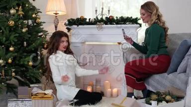 女孩制作照片手机，女朋友正在准备平安夜，女人说话，笑，坐在圣诞节附近。
