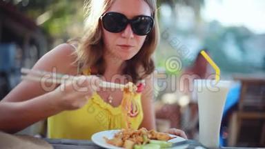 年轻优雅的幸福女人戴着太阳镜吃<strong>垫泰国</strong>炒面加鸡蛋，<strong>泰国</strong>菜。 坐在咖啡馆里