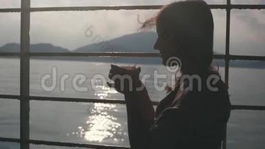 年轻的忧郁的女孩坐在货轮上的长凳上，从纸杯里喝咖啡，眺望大海。 1920x1080