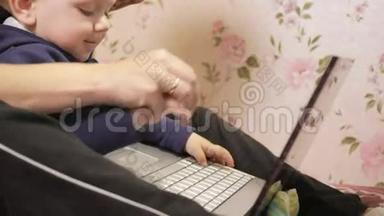 年轻女子带着儿子坐在家里的沙发上，拿着笔记本电脑。 仔细看屏幕，按下键。