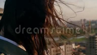 后景。 特写风吹着长长的黑发，美丽的年轻女人。 日落时站在屋顶上的女孩。 慢节奏