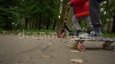 两个青少年骑滑板车和一个便士板。 他们沿着公园的小路前进。 公园里的秋日，绿色