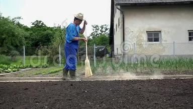 农夫在花园的小路上用一把大扫把扫地
