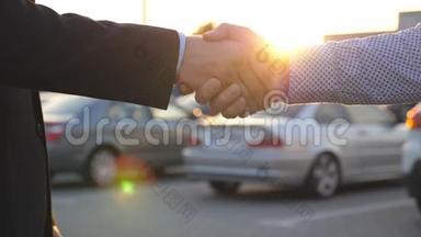 两个商人互相握手，车停在后台。 经理或经销商之间的握手