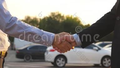 两个商人互相握手，车停在后台。 经理或经销商之间的握手