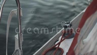 帆船板的近景.. 白色游艇溅起浪花.. 绳索固定在绞盘头周围。