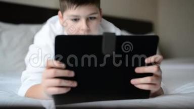 穿着<strong>白色浴袍</strong>在床上玩平板电脑的青少年
