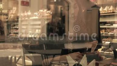 美丽的黑发女孩在糕点店喝热巧克力。 从外面透过窗户观看。 4K视频
