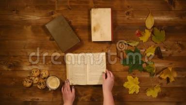 秋季概念俯视图.. 书，枫叶，烤旧的木桌.. 女人翻阅书页