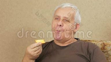 超重老人在家里的沙发上吃水果。 他切下一块柿子，咬了几口。 健康食品