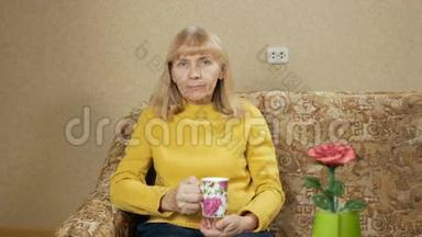 一个年老的女人在家里的沙发上喝着一杯热饮料，看着相机。 3.她辛苦了一番