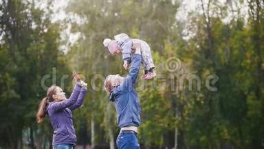幸福的家庭：爸爸、妈妈和小女孩在秋天公园散步：爸爸手里拿着婴儿，动作很慢