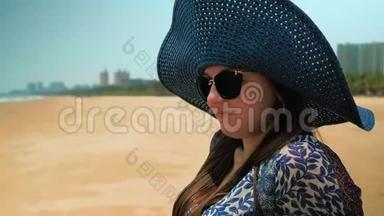 美丽的快乐女孩戴着蓝色的<strong>帽子</strong>和眼镜，坐在阳光明媚的<strong>夏日</strong>海滩上。 近距离射击。 慢动作