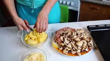 一个女人正在切土豆。 桌子旁边有切碎的蘑菇、烤盘、多汁的肉末和切碎的奶酪。