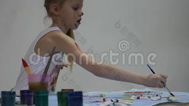 小女生。 可爱的小女孩画家在桌子上画画，在她的衣服上画画。 慢动作