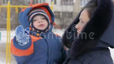 婴儿在他妈妈怀里`冬天在公园里。 他们热情地穿着衣服，母亲和她的儿子说话。 一个英俊的男孩