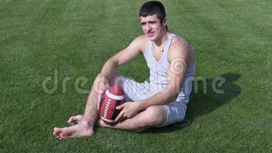 年轻运动员带着橄榄球坐在草地上