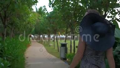 戴着蓝帽子的年轻女孩正穿过一个热带公园。 夏日时光。 慢动作。