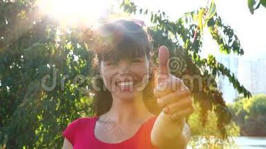 美丽的笑女在公园里竖起大拇指，背景是阳光