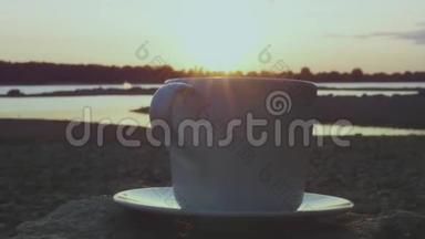 一杯美味的热茶或咖啡放在一块大石头上，日落时在河边用蒸汽。 高清，1920x1080。 慢动作。