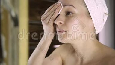 穿毛巾的漂亮女人在镜子前卸妆。 家庭水疗中心