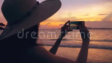 海洋海滩日落时分，戴帽子的年轻游客<strong>女士</strong>用手机拍照<strong>剪影</strong>