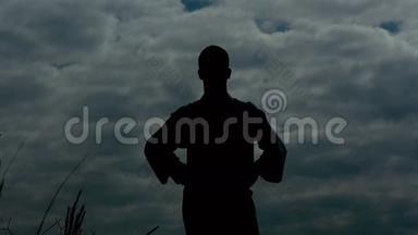 人类的Silhouete站在岩石上，举起手臂在天空背景上。 慢慢地
