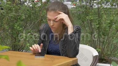悲伤的漂亮女孩坐在咖啡馆的桌子旁。 在智能手机上读取短信。 悲伤和渴望，绝望。