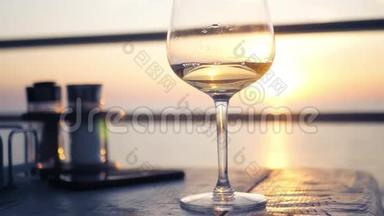 桌上放着一杯白葡萄酒，背景是夕阳和地平线上的大海。 高清，1920x1080
