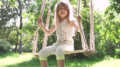 小女孩在夏天公园的秋千上摇摆。 在树上的绳子上摆动。 快乐无忧无虑的童年。 慢慢慢慢