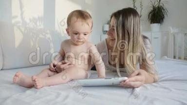 美丽的年轻母亲和她的小儿子在卧室里看数码平板上的卡通片