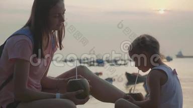 旅行者的母亲和女儿坐在海边，在旅途中喝椰子
