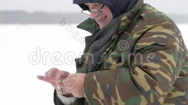 那个人在冰上钓鱼钓到一条小鱼。 他把它从钩子上拿下来扔到冰上。 穿着防护衣