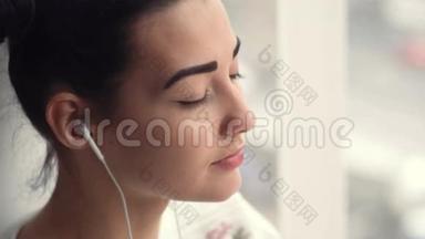 戴着耳机坐在窗边听音乐的迷人年轻女子