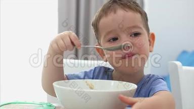 小<strong>可爱</strong>的孩子正坐在一张桌子旁<strong>吃</strong>着自己的燕麦片，<strong>宝宝吃</strong>得心甘情愿.. 快乐童年的概念。