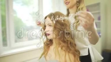 专业发型师沙龙理发师将珠宝首饰上的饰毛戴冠珍珠皇冠戴在金发波浪型女模特头上