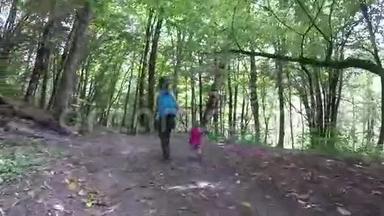 妈妈带着一个粉红色的背包在树林里牵着女儿的手。 健康的生活方式。 家庭在户外的树林里散步