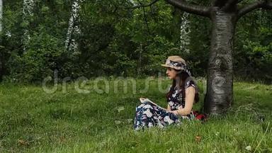 穿着衣服戴帽子的漂亮女孩正在农村度假时在树下看书。