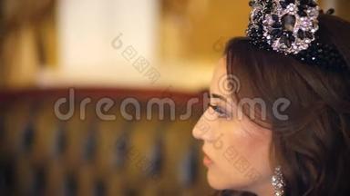 一个美丽的女孩，穿着一件长裙，化妆和皇冠，在经典的室内为摄影师摆姿势