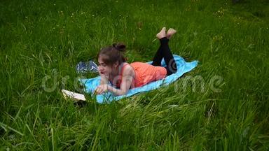 轻松的小女孩在田里看书。 可爱的少年躺在草地上。 视频镜头高清拍摄静态