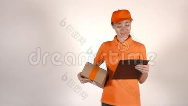 漂亮的女<strong>快递</strong>员穿着橙色制服<strong>送</strong>包裹。 浅灰色背景，4K摄影棚拍摄